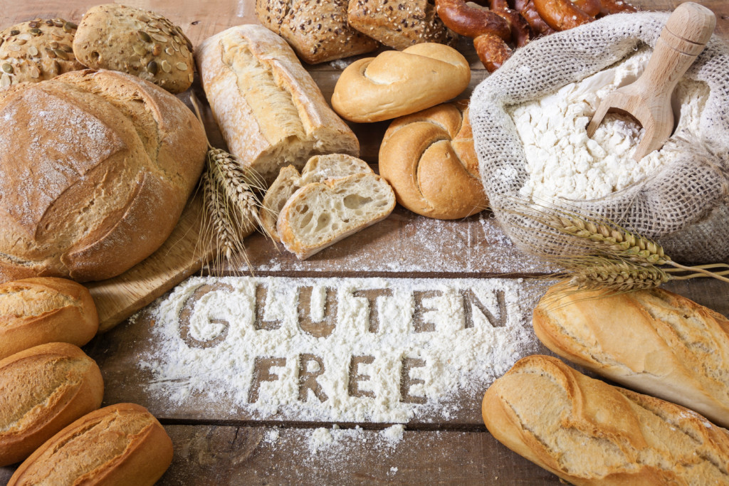 Verschiedene Gluten, glutenhaltige Lebensmittel, darunter Brot, Kekse und Pasta, auf einem Tisch arrangiert, mit einem 'glutenfrei' Etikett im Vordergrund.