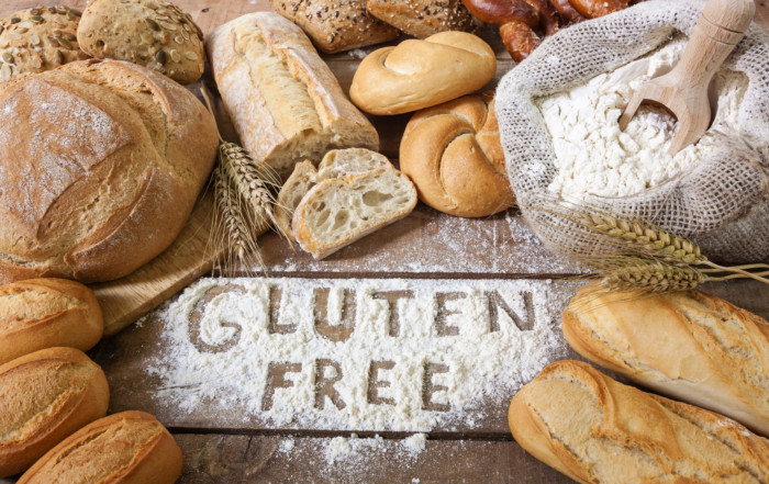 Verschiedene Gluten, glutenhaltige Lebensmittel, darunter Brot, Kekse und Pasta, auf einem Tisch arrangiert, mit einem 'glutenfrei' Etikett im Vordergrund.