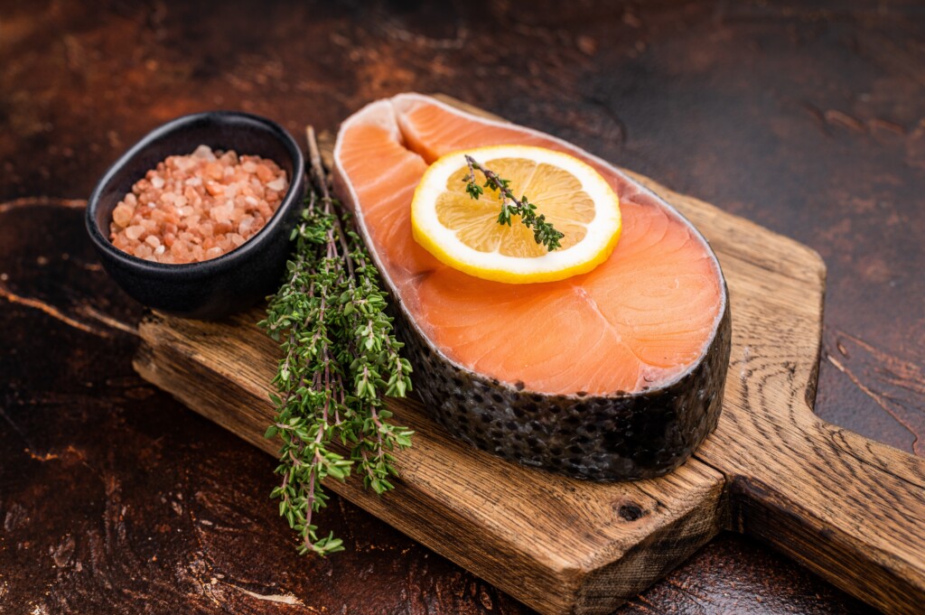 Roher Lachs auf Holzbrett mit Zitrone und Kräuter.